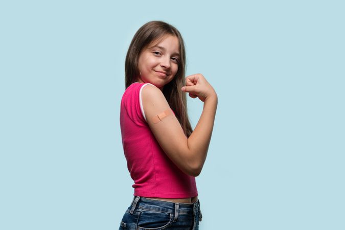 Young girl proudly flexing arm with bandage after vaccination