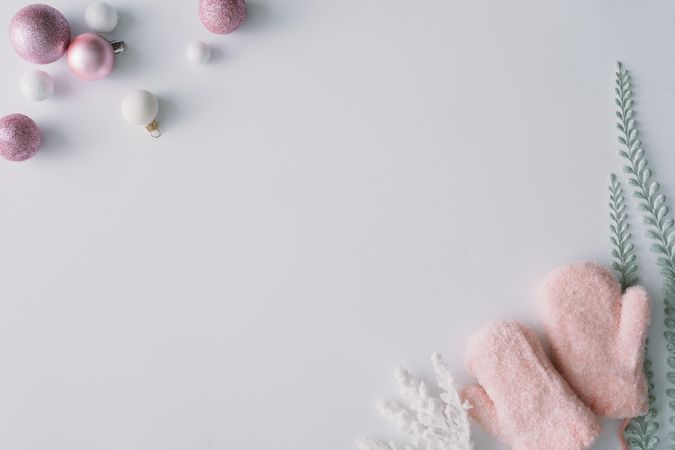 Pink baubles and mittens with snowy leaves in corners of light background