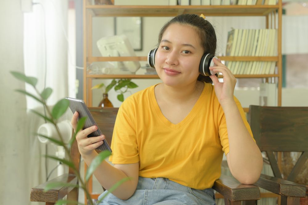 Young woman in the yellow shirt is listening to music  an app on smartphone at home.