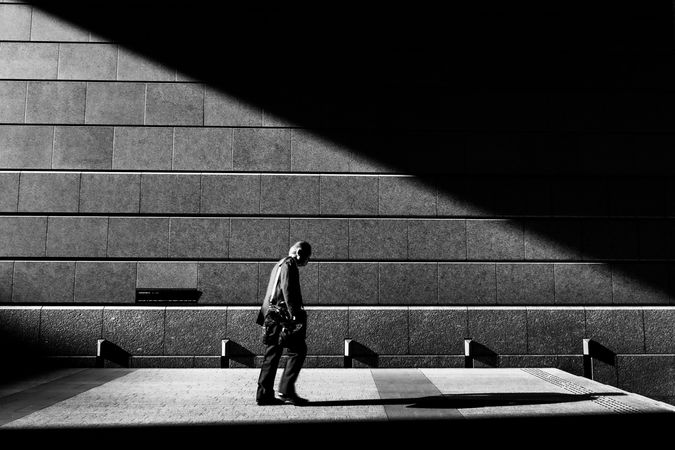 Grayscale photo of an older man walking beside wall