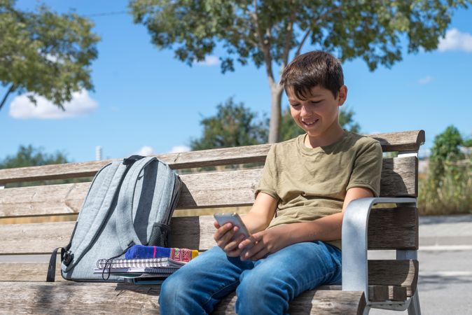 Happy teenage boy looking at phone on bench