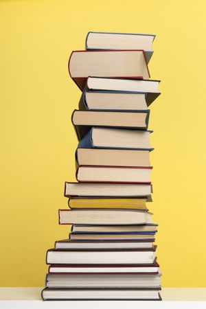 Pile of books stacked on a yellow background with space for copy in a vertical image
