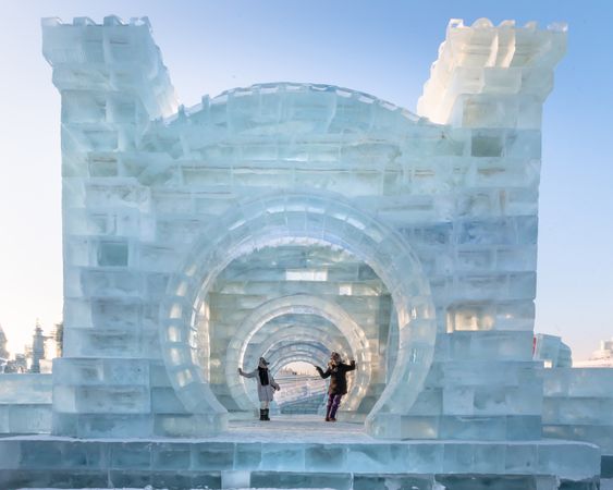 man and woman in warm outwear standing standing on illuminated castle of ice and snow