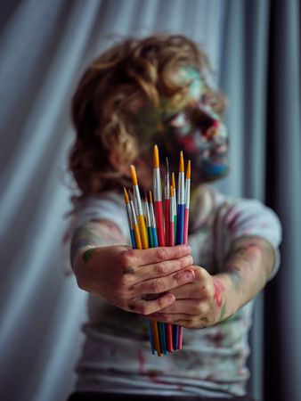 Messy boy showing set of paintbrushes