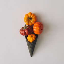 Pumpkins in ice cream cone on light background