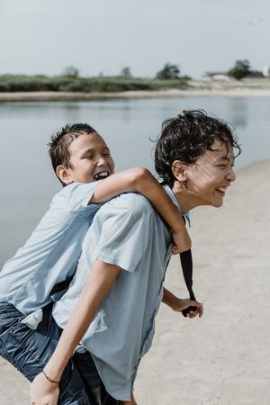 Boy carrying younger brother in piggyback ride by pond