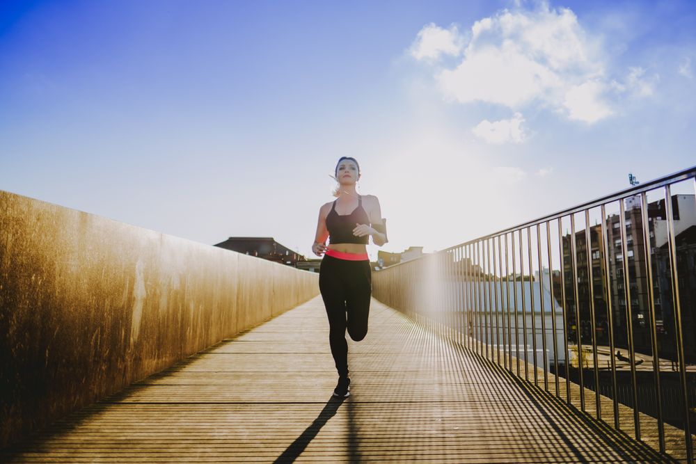Woman running on walkway in sunny day with blue sky