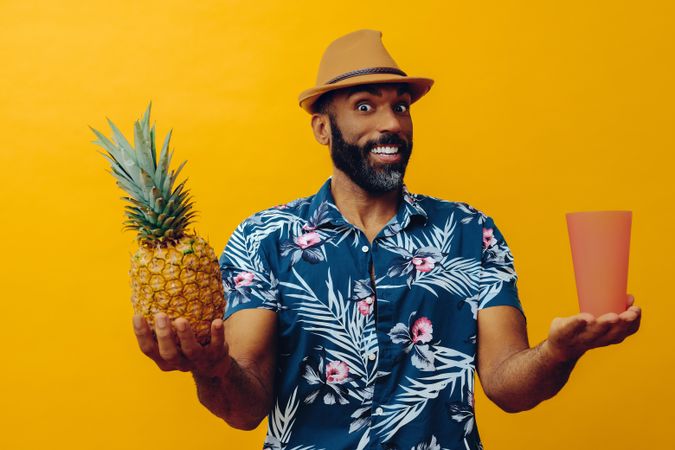 Smiling male holding up a pineapple and orange cup