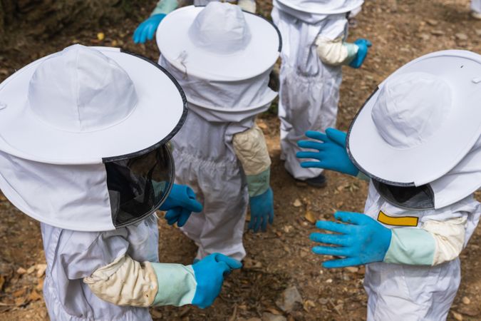 Faceless group of children in protective uniform in apiary