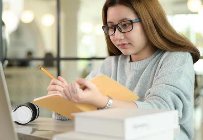 Young woman with a pen and a notebook is taking notes from laptop