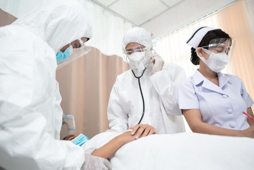Medical staff in full PPE taking heart rate of patient lying in bed