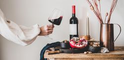 Rustic setting of women swirling wine, with cheese, long candles, pomegranate, and dried poppies