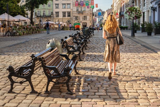 Back view of woman walking on street near bench in Lviv, Ukraine