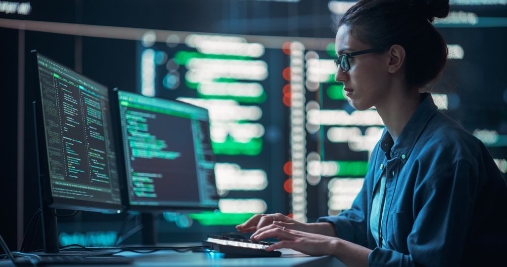 Medium Shot of a Woman Working as a Developer, Surrounded by Big Screens Displaying Lines of Code in a Monitoring Room.