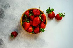 Looking down at strawberries in wooden bowl full on grey counter with copy space