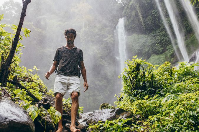 Young man hiking in forest with waterfall in background