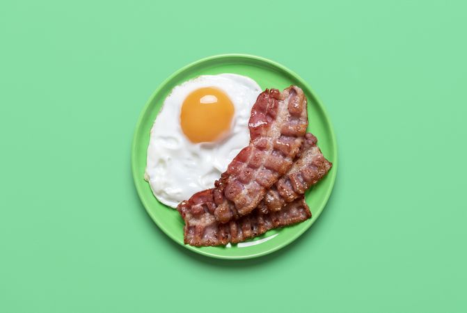 Fried egg and bacon on a green background, above view