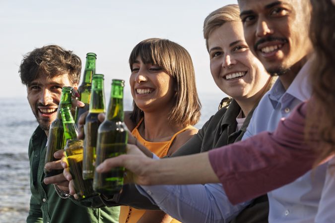 Close-up of diverse friends cheering with beer bottles at seaside summer party