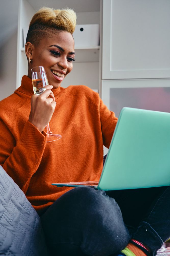 Black woman talking on a video call on her a laptop with champagne flute in a modern studio