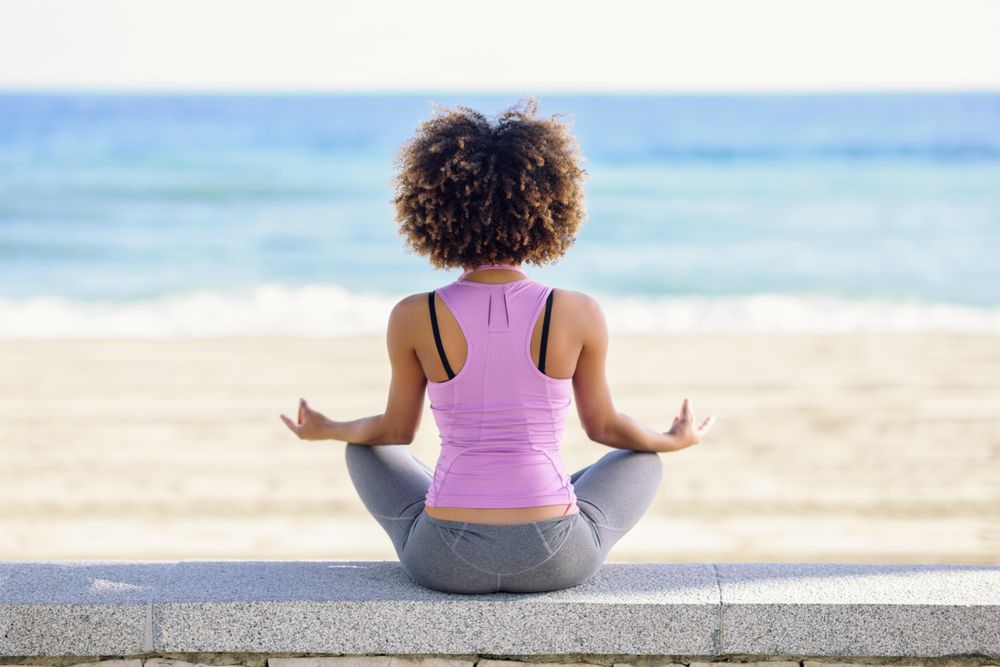 Back of Black woman with afro hairstyle meditating on the beach