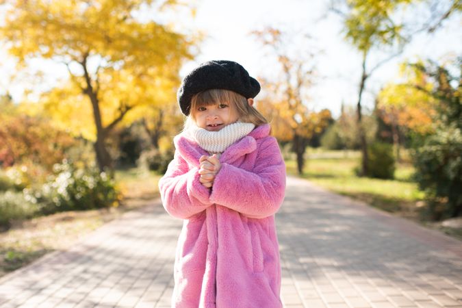 Girl in pink coat standing near autumn trees in park
