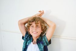 Cheerful boy with raised arms against wall