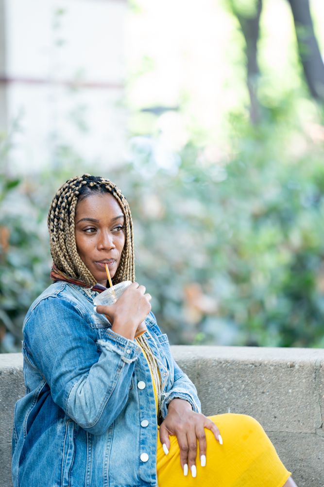 Woman drinking to-go iced coffee with straw smiling and looking away