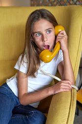 Astonished girl talking on retro telephone in room