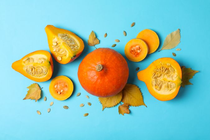 Composition with pumpkin, slices, leaves and seeds on blue background
