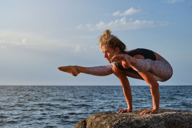 Fit woman balancing on arms while practicing yoga asana on stone