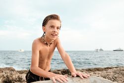 Shirtless boy wearing shell necklace looking away at beach