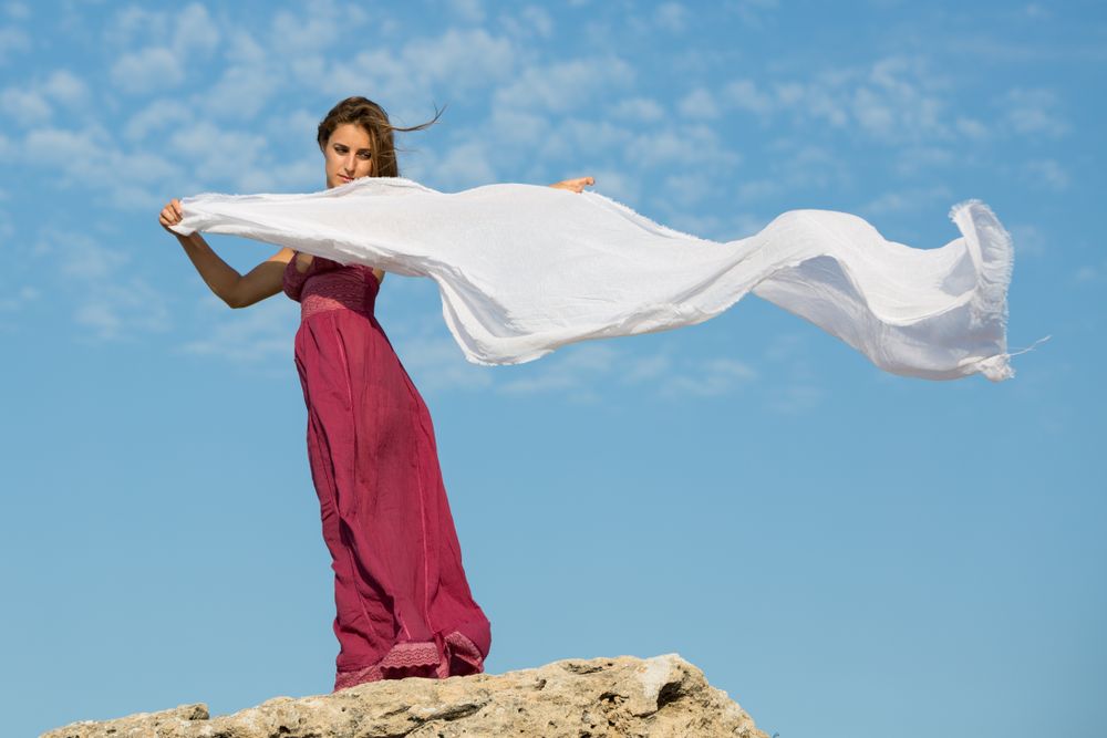 Woman in dress with scarf in upped hands near stone monument