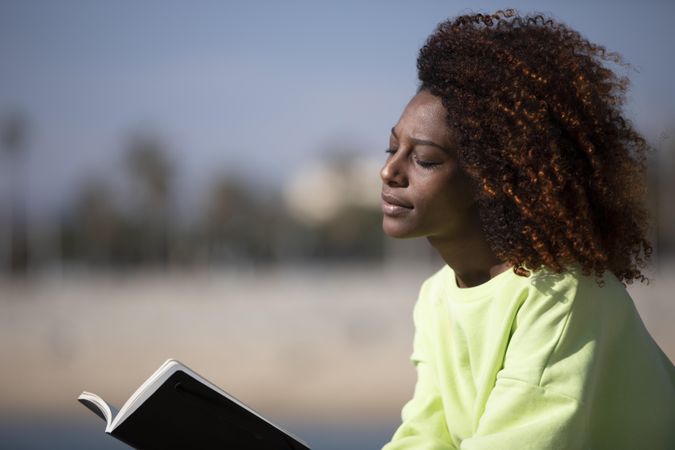 Female in bright green shirt relaxing on the seaside on sunny day with a book
