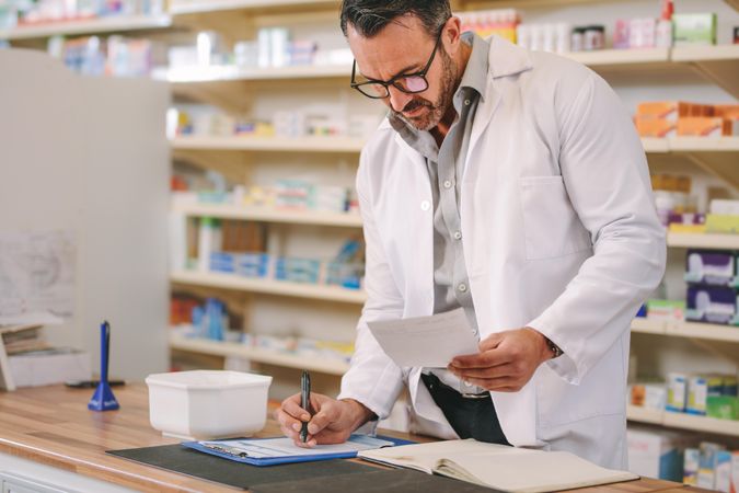 Male pharmacist writing prescription pharmacy counter