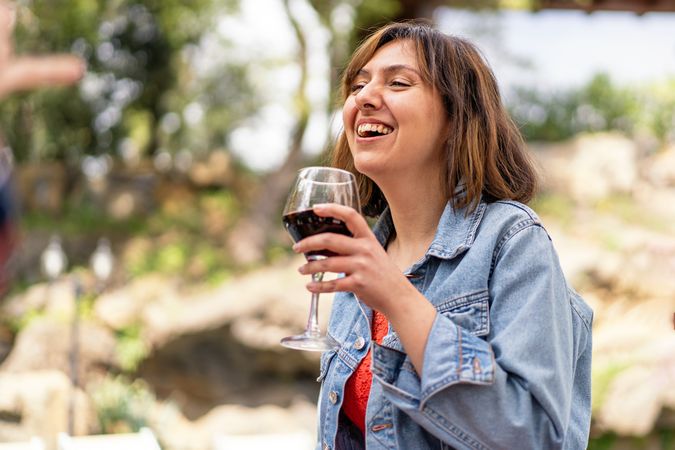 Laughing woman taking a sip from a glass of red wine outside
