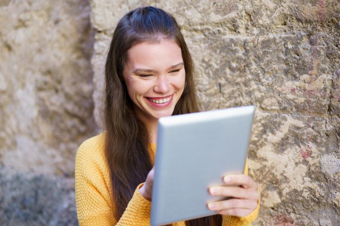 A Joyful Young Woman Happily Using a Tablet While Relaxing in an Outdoor Setting