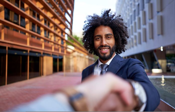 happy businessman shaking hands with partner and looking at camera