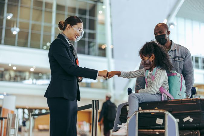 Ground staff at airport terminal greeting girl in face mask with her father during pandemic