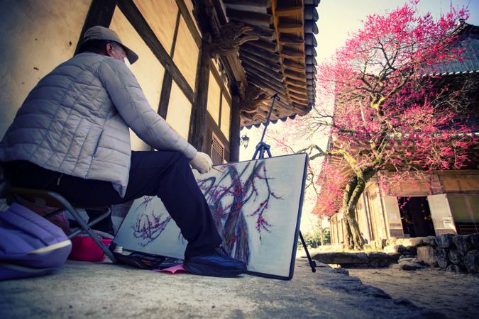 Back view of an older man drawing a cherry blossom tree outdoor