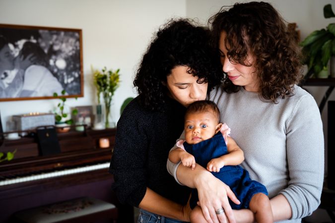 Happy couple at home with their newborn with one mom kissing the top of the baby’s head
