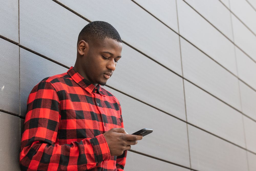Serious Black man using smartphone against gray wall