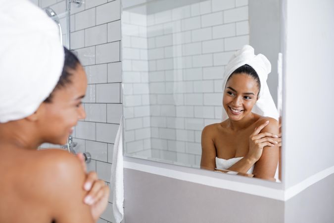 Radiant woman in towel touching her shoulder in the mirror