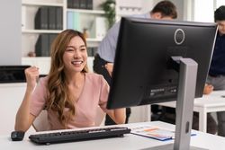 Asian woman making fists with her arms up in celebration while sitting at her desk