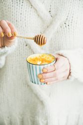 Cropped shot of female using honey dipper to add sugar to latte