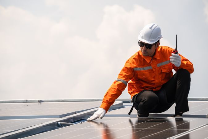 Male engineer checking solar cell  or photovoltaic cell by electronic device installed on the roof of the factory. Technician worker repair or inspect the system. Industrial renewable energy concept