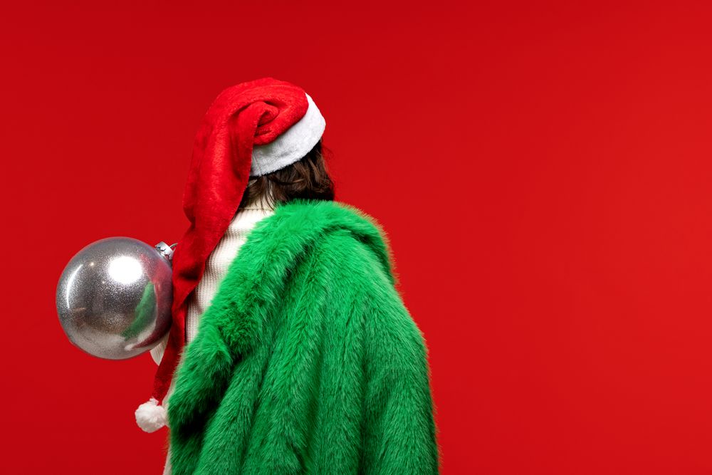 Woman in Santa hat and green coat carrying silver ornament.