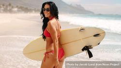 Woman in bikini and sunglasses with surfboard on beach 4A3oW0