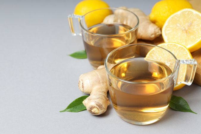 Cups of tea, ginger and lemons on gray background, space for text