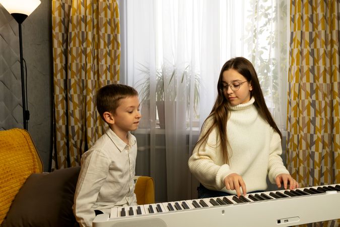 Young girl teaching boy to play the piano