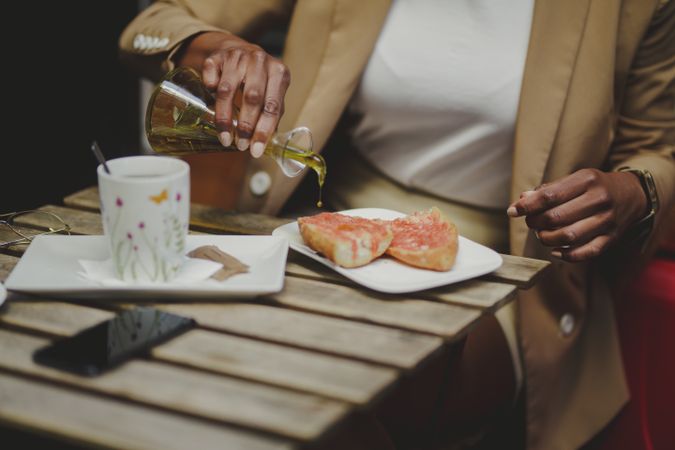 Black woman pouring oil on sandwiches at table with smartphone in cafe